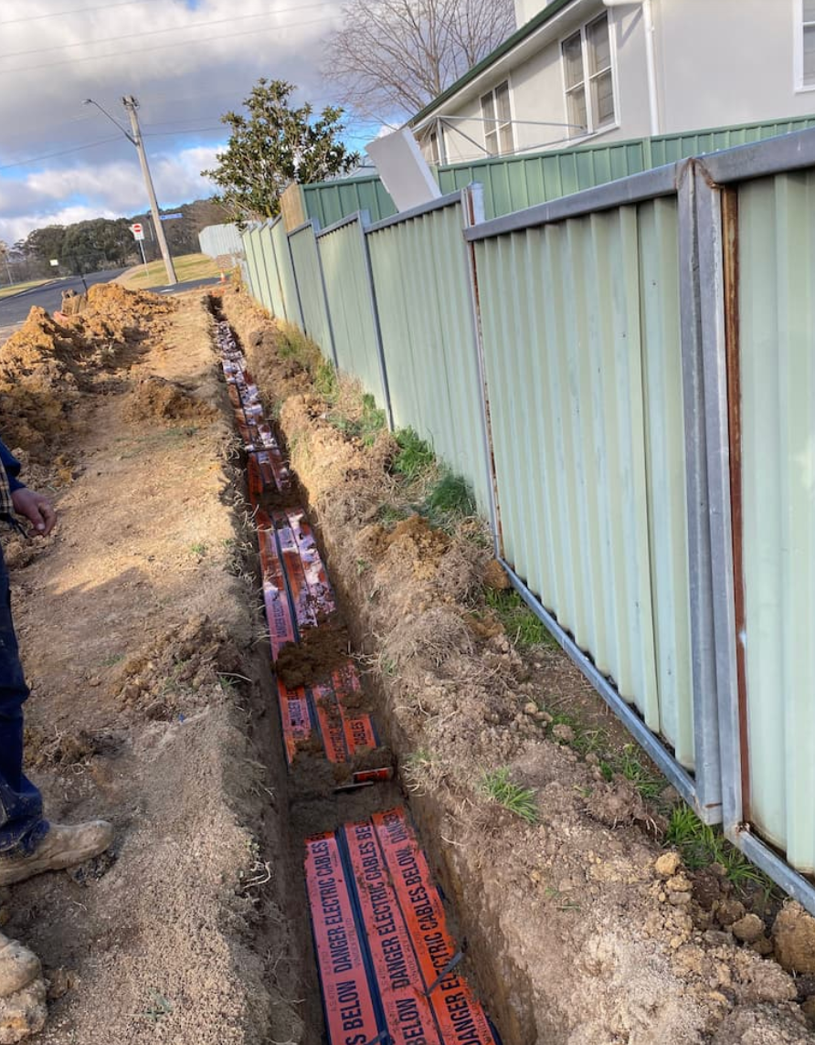 A power cable is being laid into the ground with a fence to the right — Central West Power Construction in Orange, NSW
