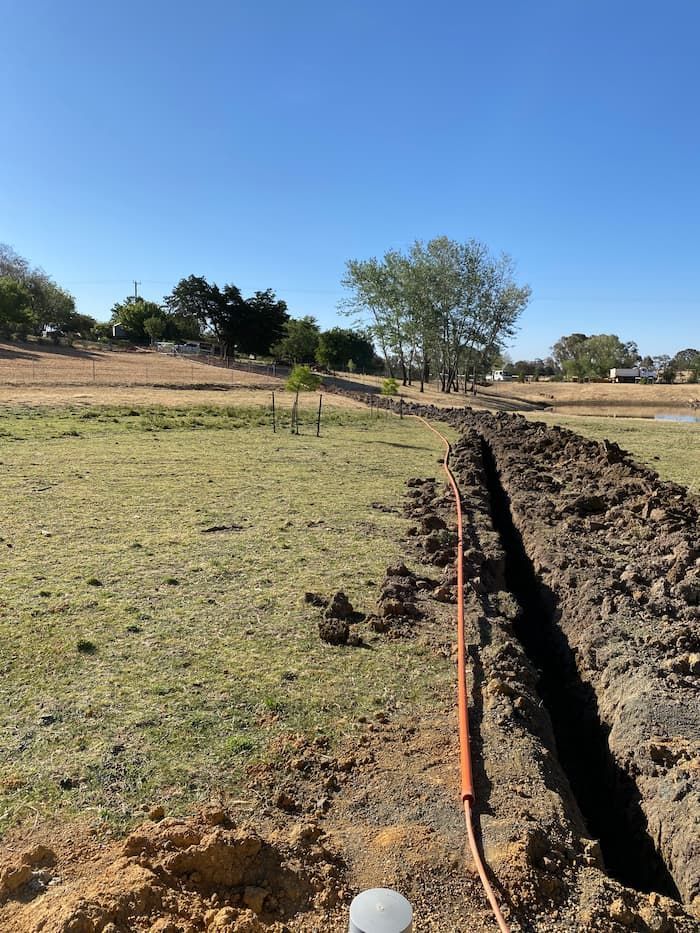 Freshly Dug Trench in a Grassy Field With Orange Conduit, Under a Blue Sky — Central West Power Construction in Orange, NSW