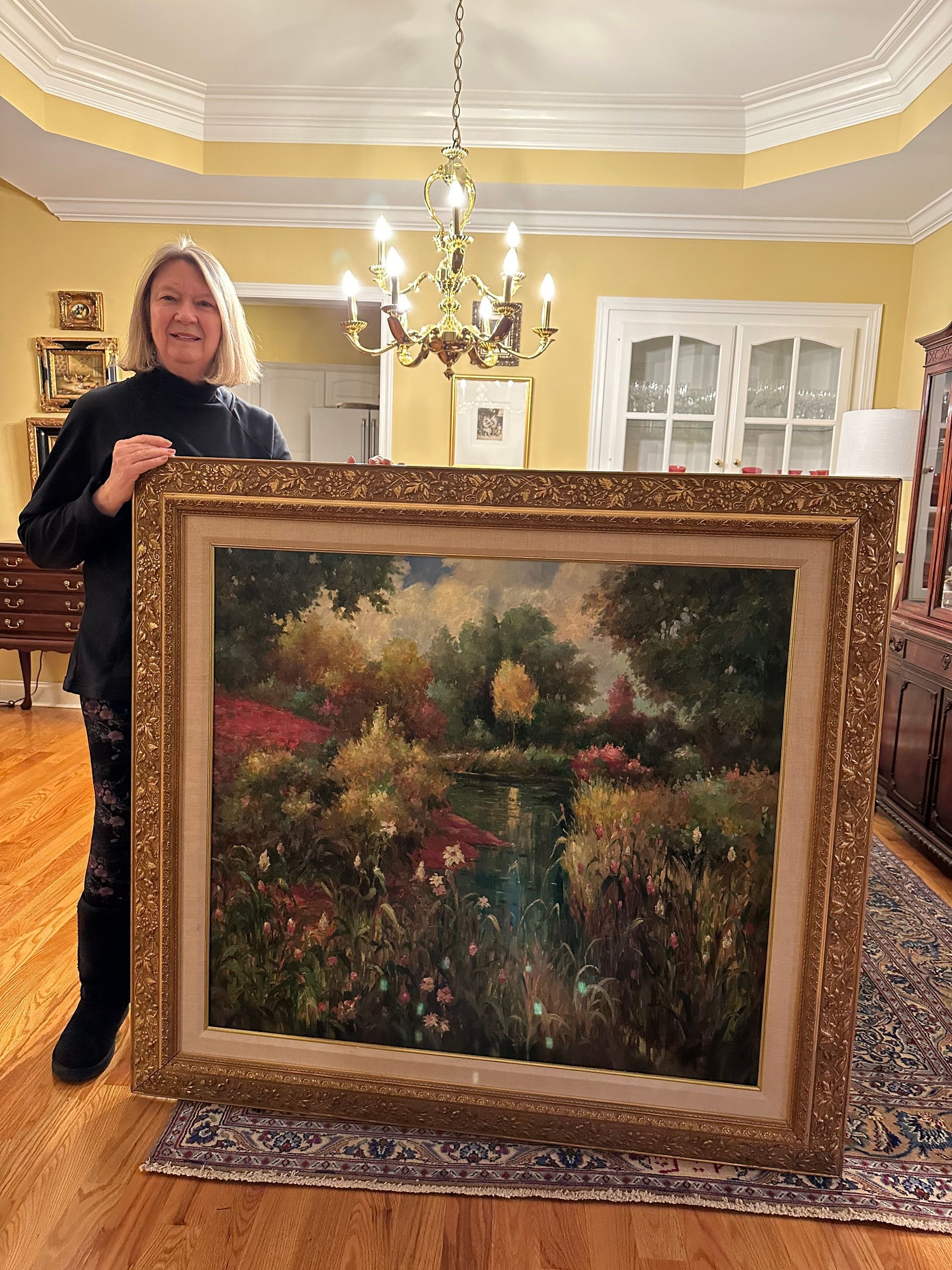 a woman is holding a large framed painting in a living room — Tampa, FL — Antique Restoration and Design
