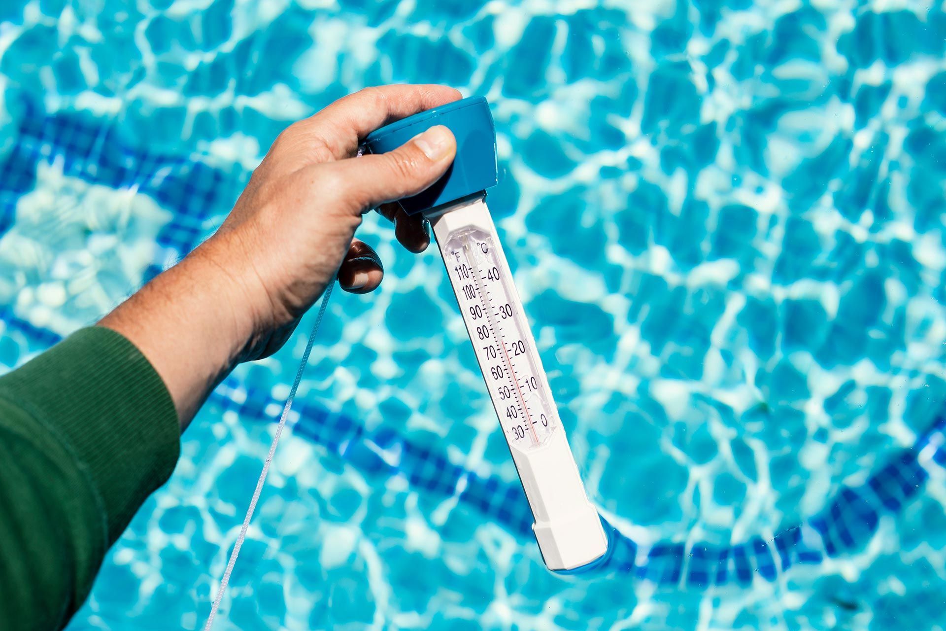 Close-up of a technician holding a pool thermometer to measure the temperature of pool water.