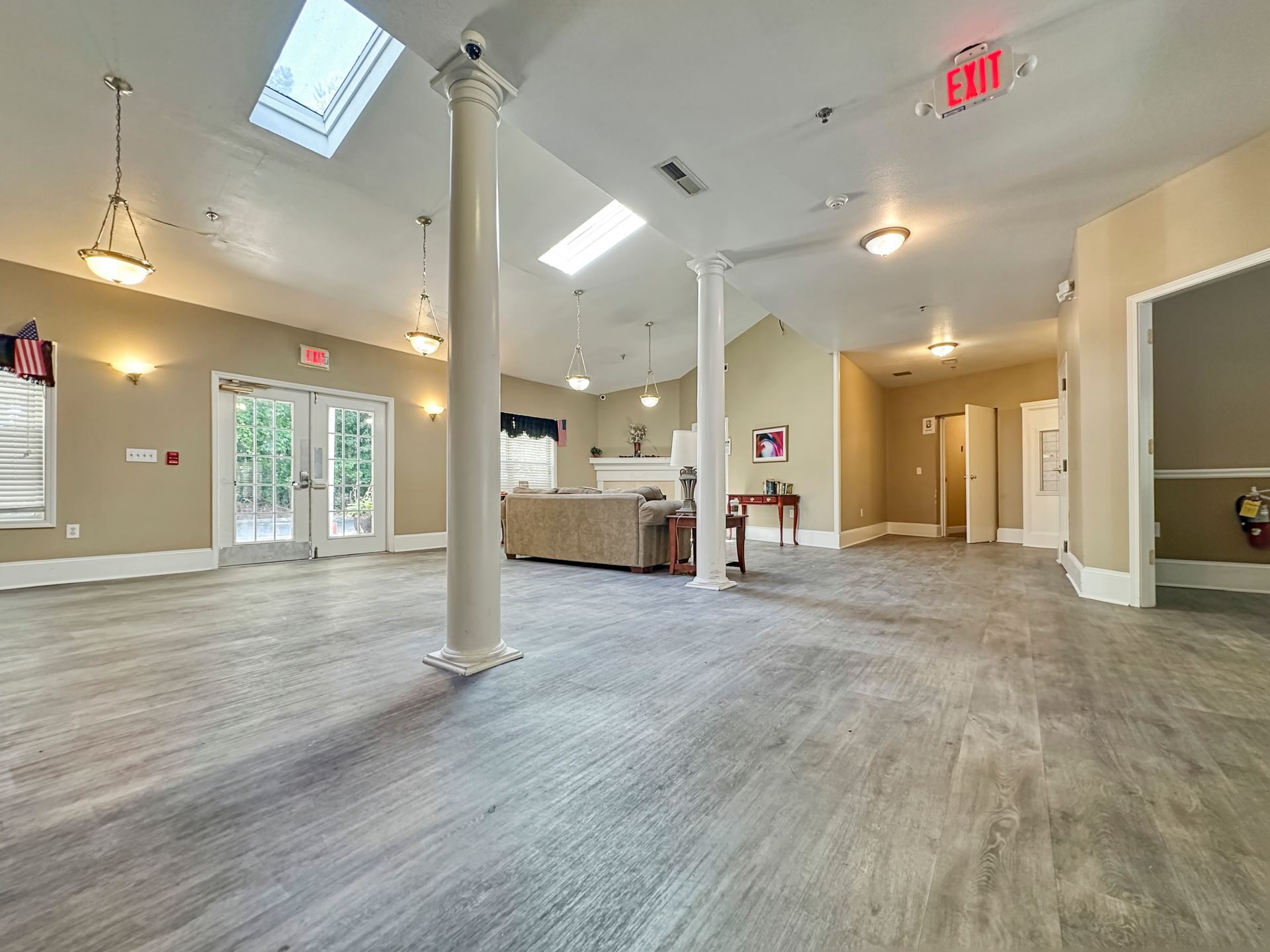 A large empty room with hardwood floors and a red exit sign.