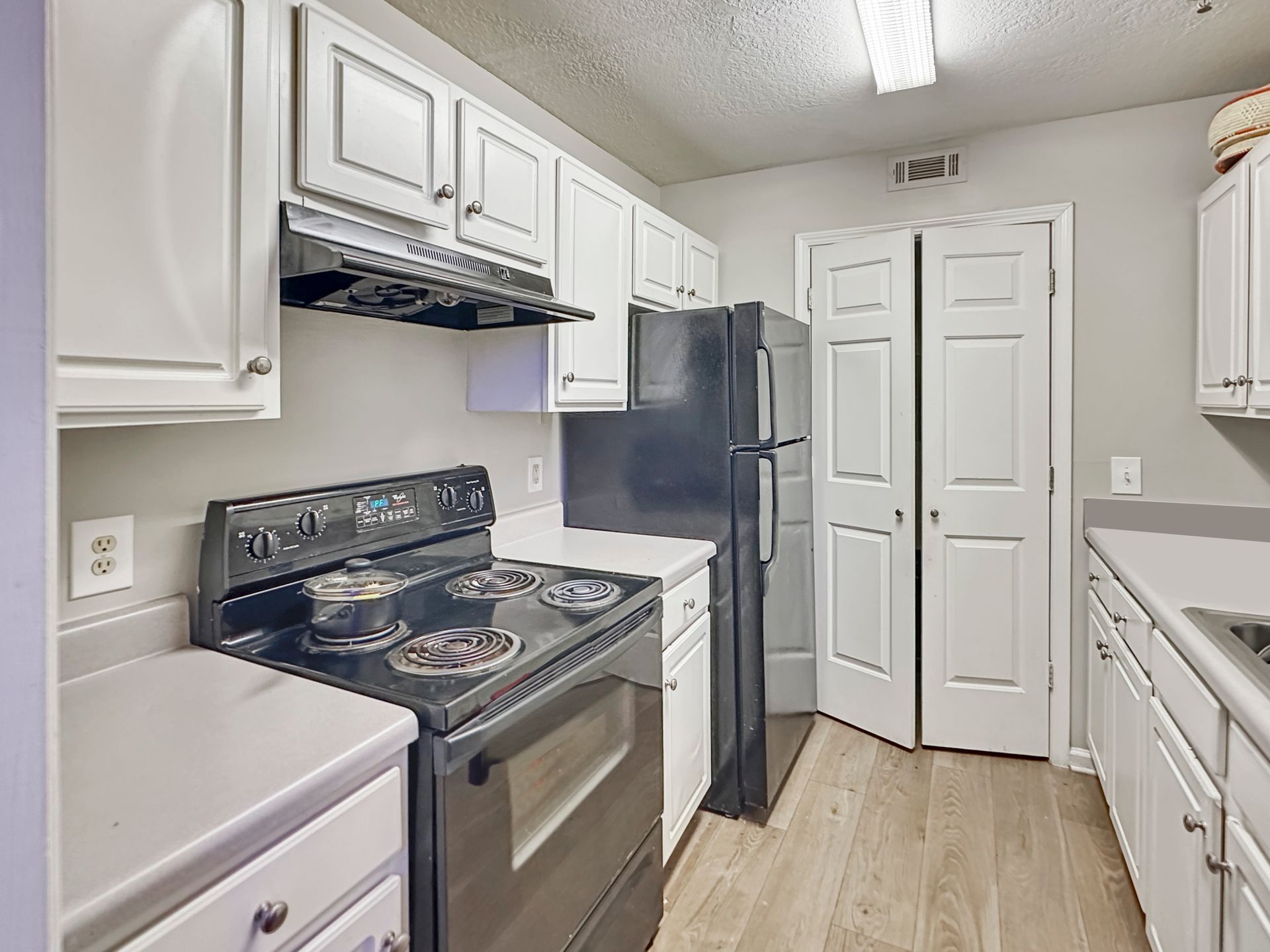 A kitchen with white cabinets , a stove , a refrigerator , and a sink.