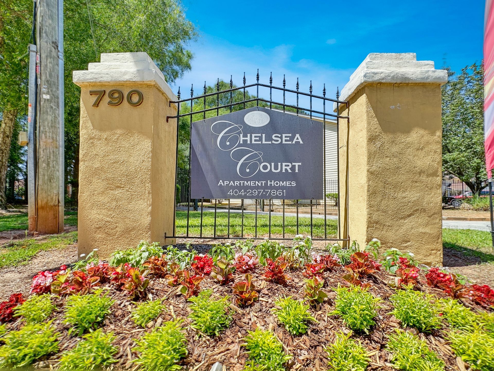 A sign for chelsea court is surrounded by flowers and a fence.