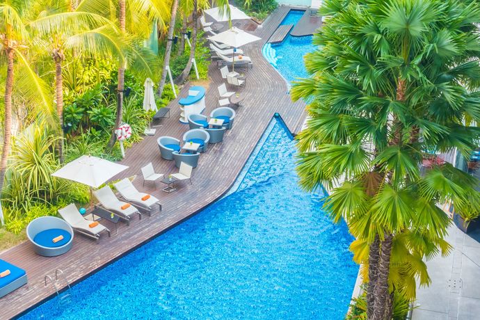 Resort pool with blue water, lounge chairs, and tropical palm trees alongside a curved deck