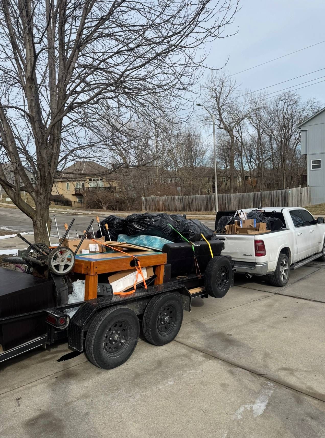 A white pickup truck pulling a dual-axle trailer loaded with furniture, boxes, and items covered in black tarps.