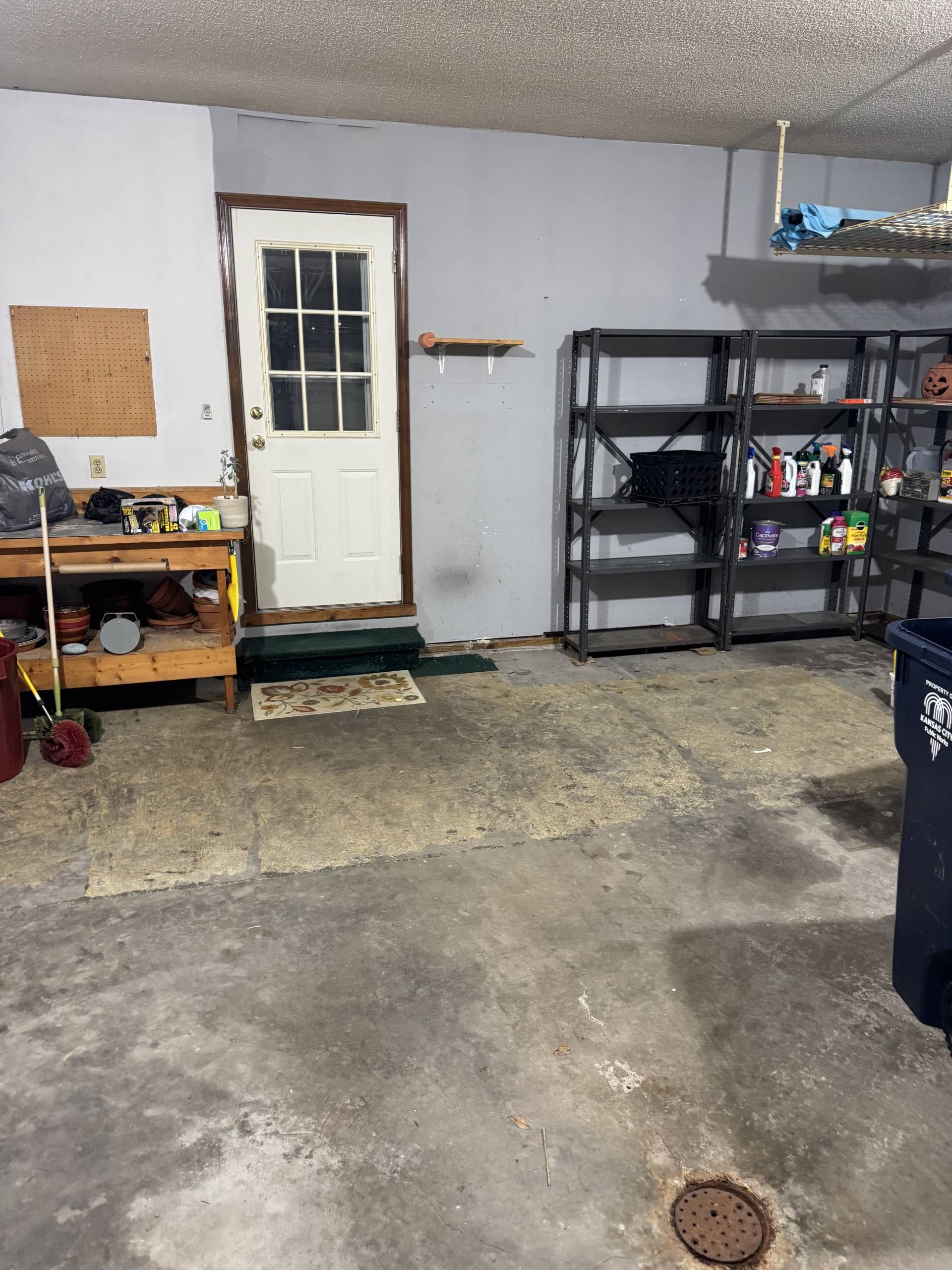 A garage interior with a wooden workbench, a white door, and black metal shelving units against a grey wall.