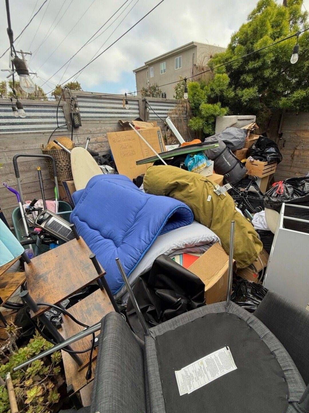 A collection of discarded items, including a blue mattress, an ironing board, and furniture, piled in an outdoor area.