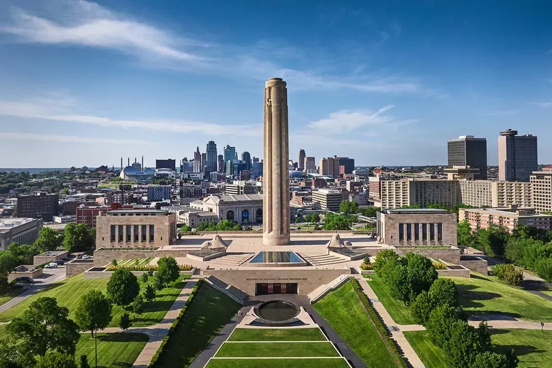 Aerial view of the National WWI Museum and Memorial with a tall central tower, stone buildings, and Kansas City skyline.
