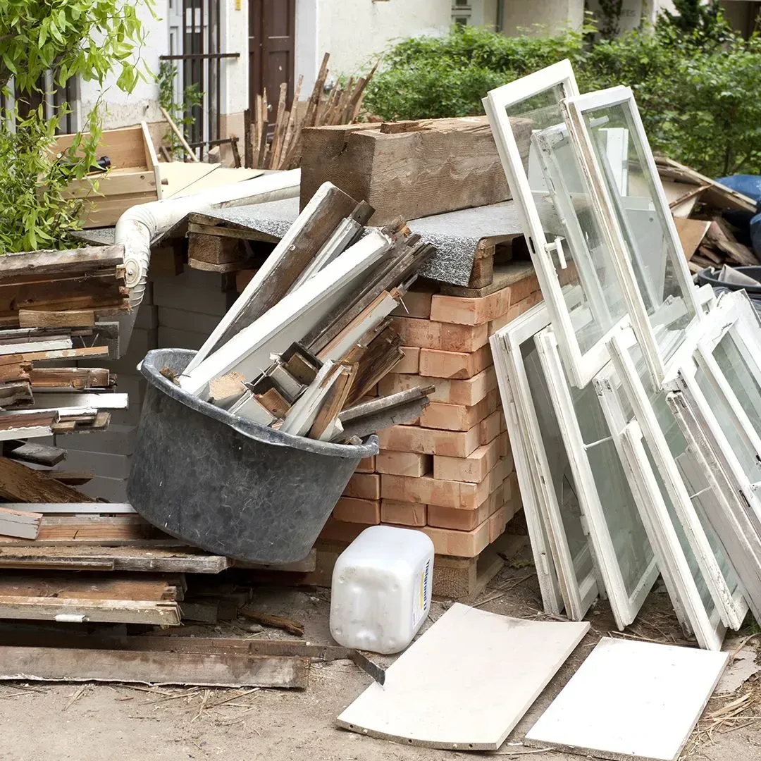 Construction waste, including window frames, a bucket of debris, and bricks, stacked outdoors.