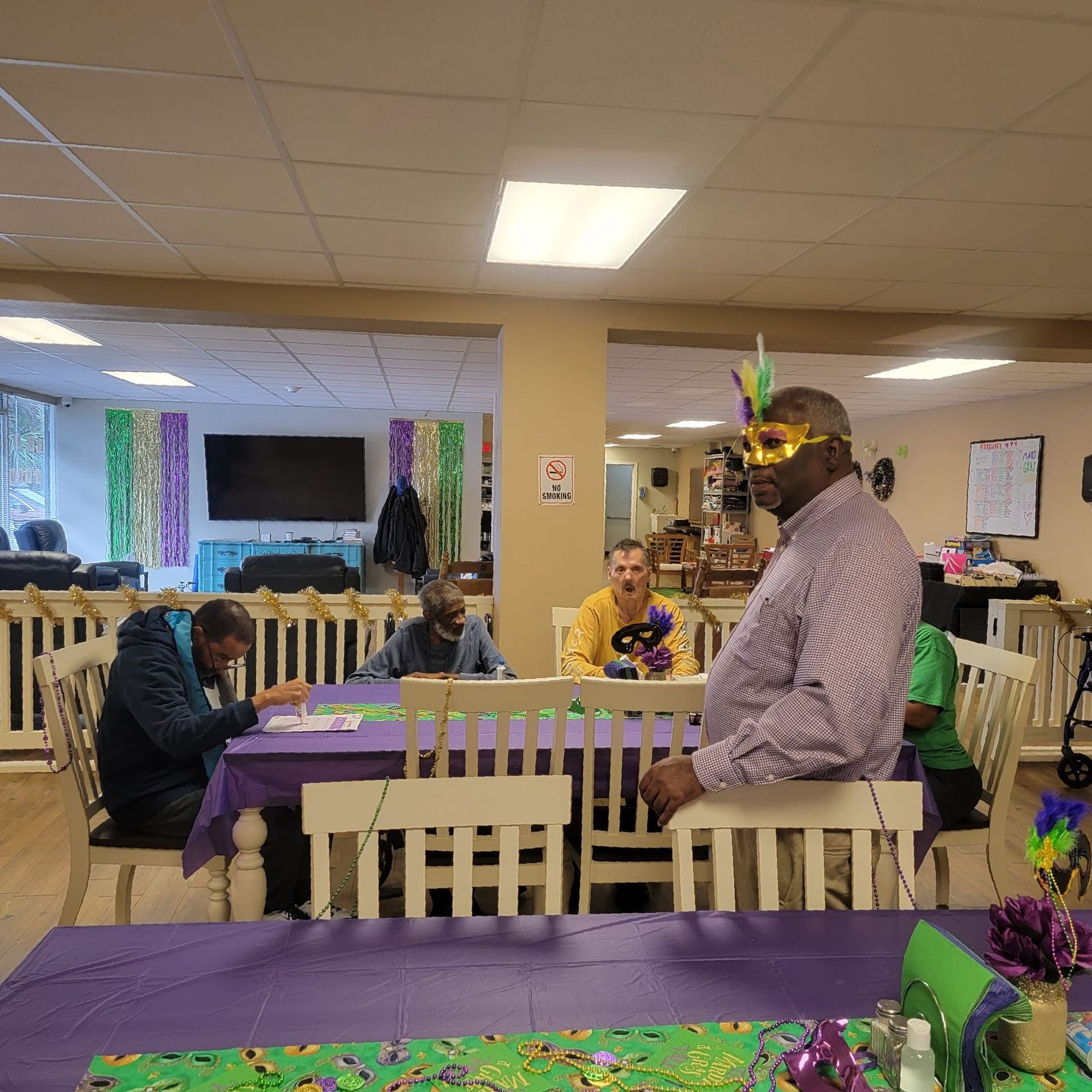A man wearing a mask is standing in front of a group of people sitting at tables.