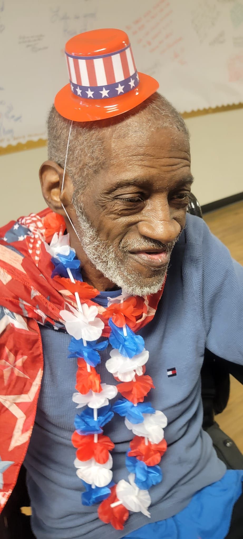 A man in a wheelchair is wearing an uncle sam hat and a lei.