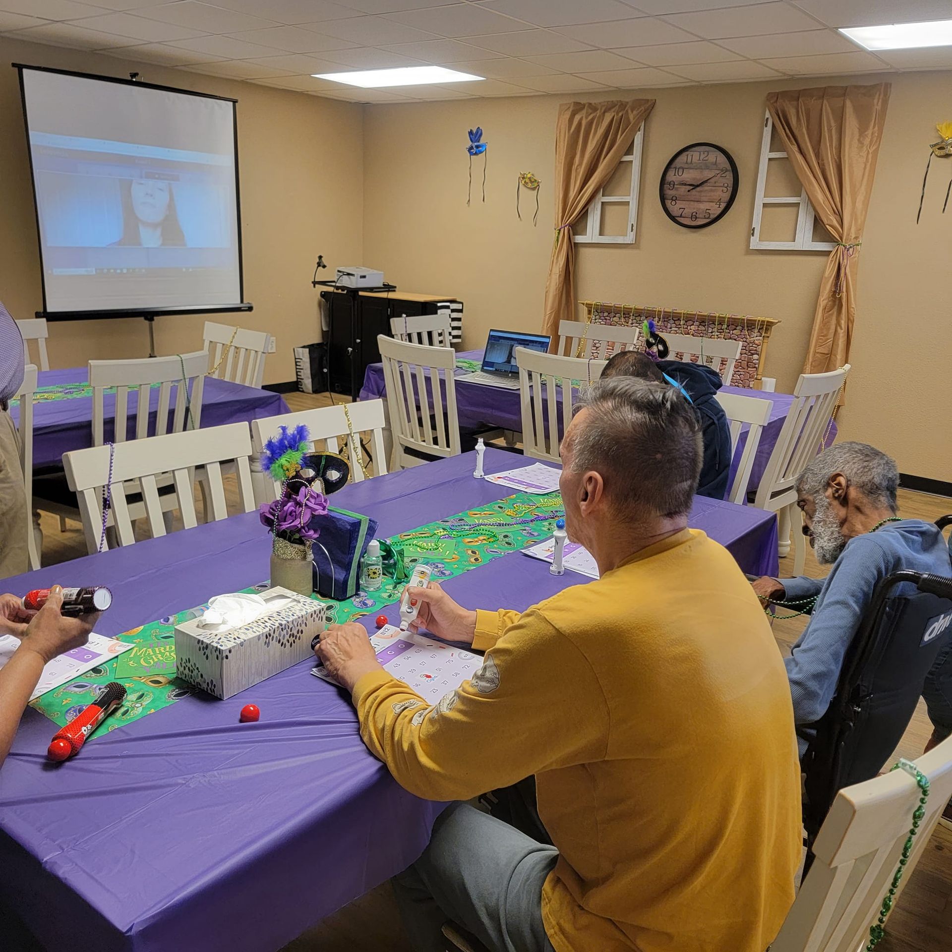 A group of people are sitting at tables in front of a projector screen.