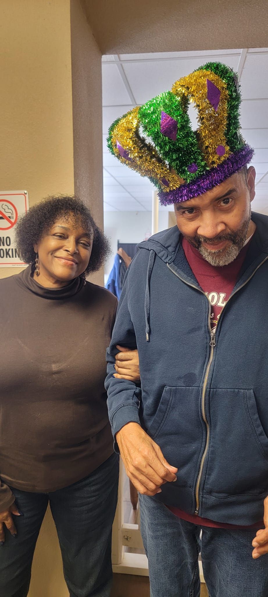 A man wearing a mardi gras hat is standing next to a woman.