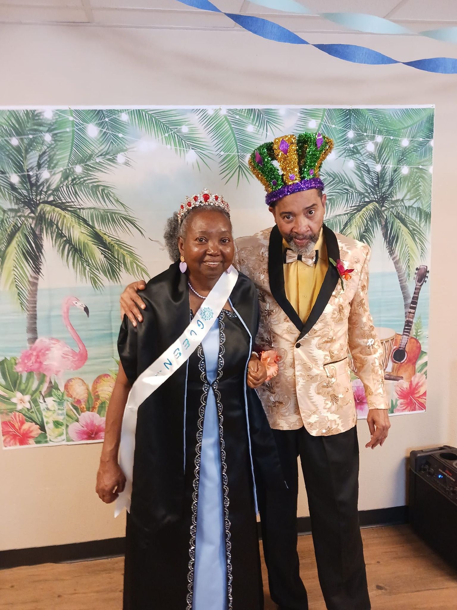 A man and a woman are posing for a picture in front of a tropical background.