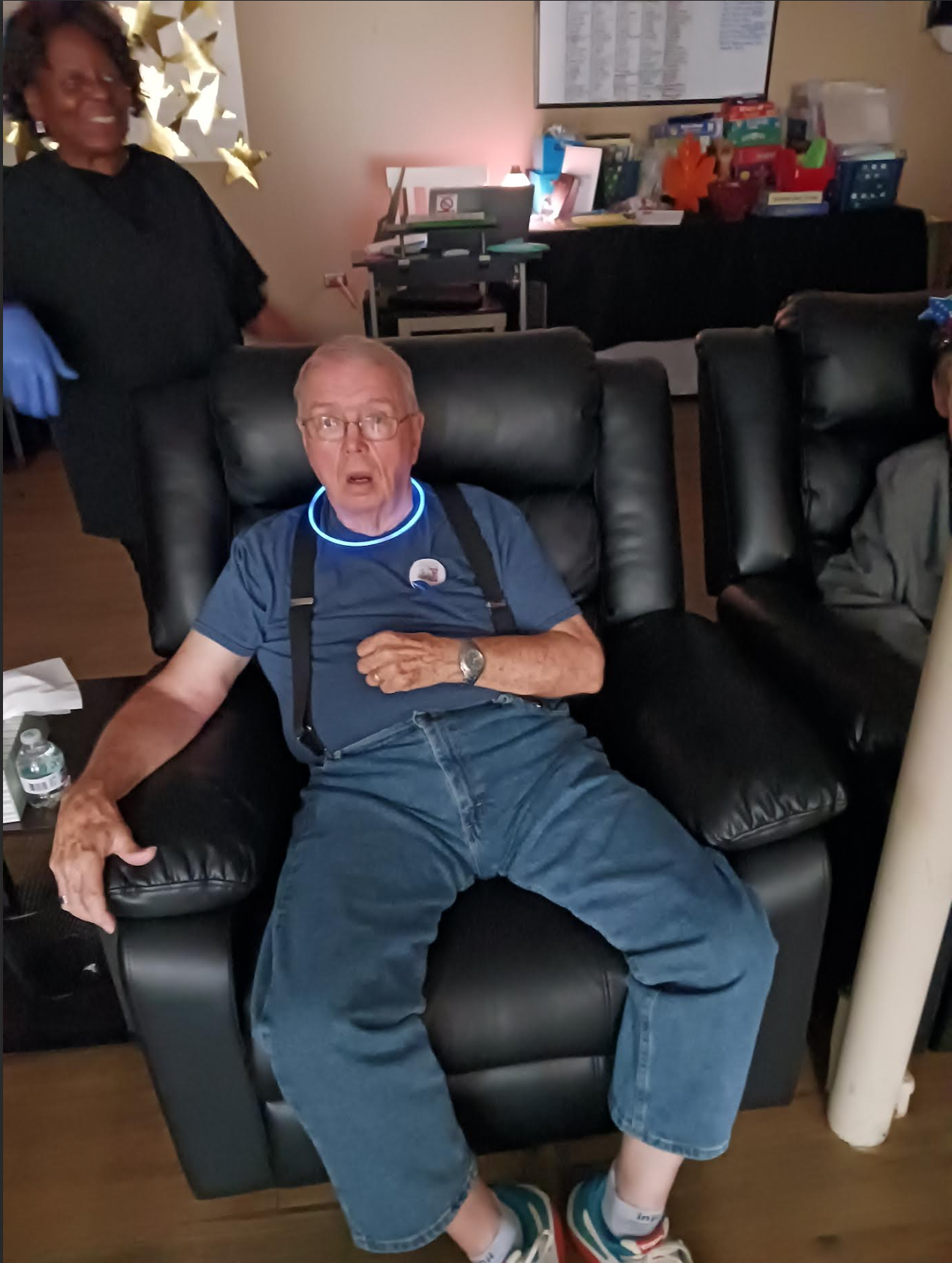 An elderly man is sitting in a black leather recliner in a living room.