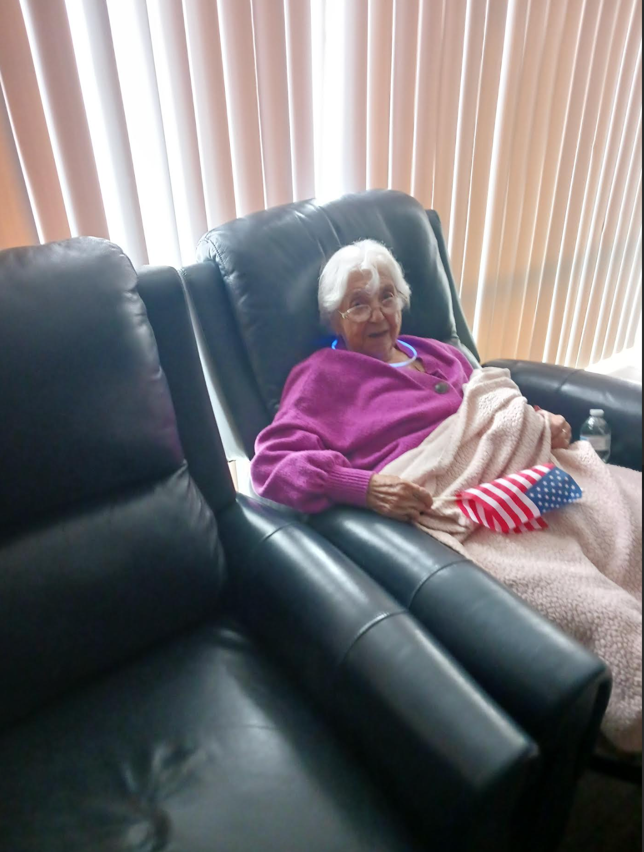 An elderly woman is sitting in a chair with an american flag on her lap.