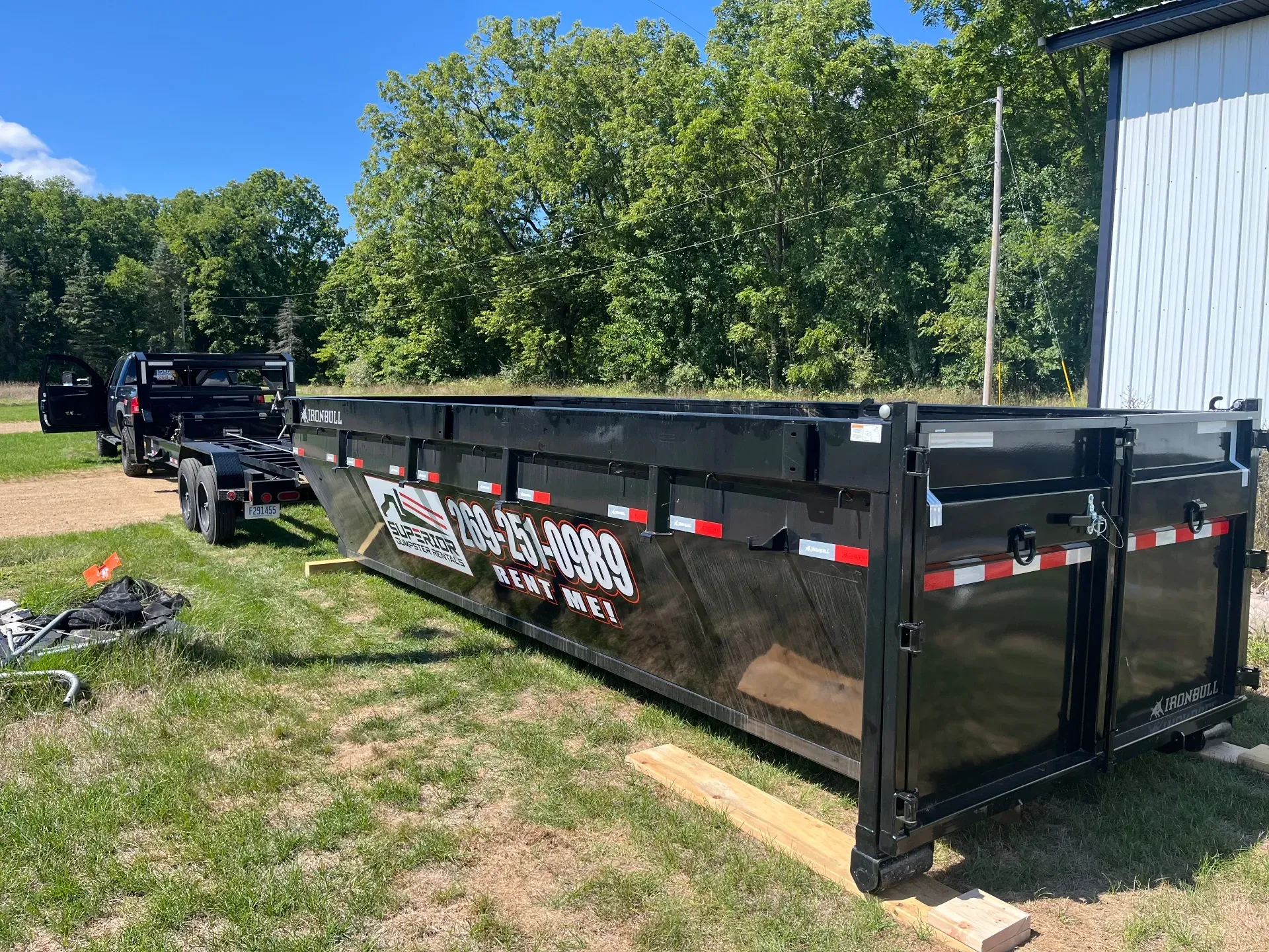 Dumpsters and truck parked on a cracked concrete lot, trees in the background.