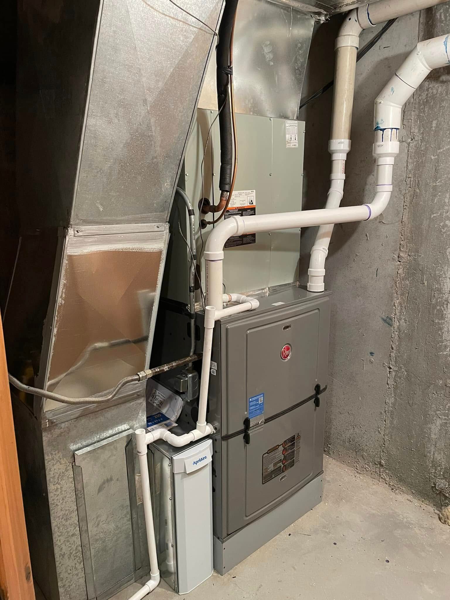 Furnace unit in a basement, with ductwork and PVC pipes, set against a concrete wall.