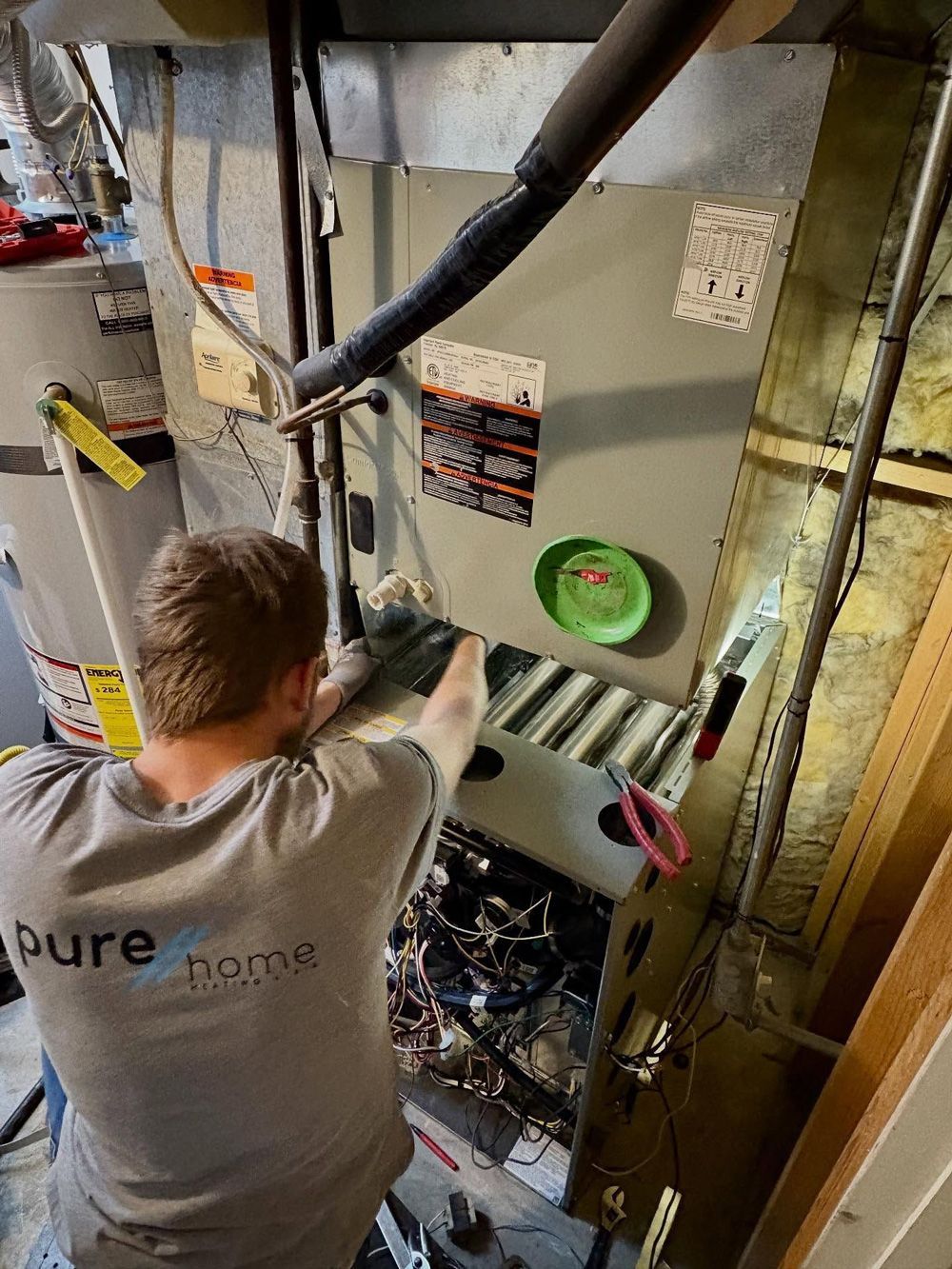 A technician repairs a furnace in a basement, wearing a gray shirt. A technician repairs a furnace in a basement, wearing a gray shirt.