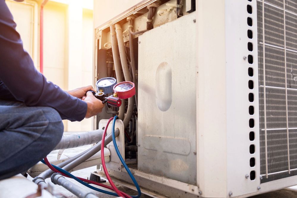 HVAC technician servicing an air conditioning unit; uses gauges and tools in a bright, outdoor setting.