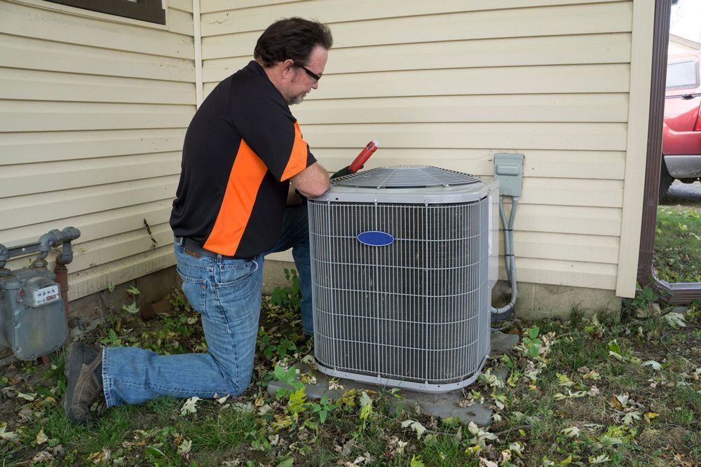 Person using a screwdriver to adjust a white radiator thermostat on a wall above a wood floor.