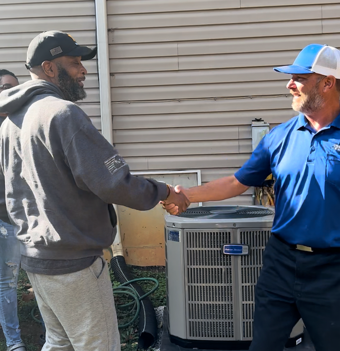 Man in white shirt and camo hat working on an outdoor Carrier air conditioning unit, on a rooftop.