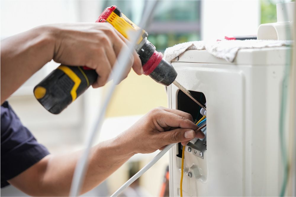 Person using a power drill to connect wires on an air conditioner unit outside.