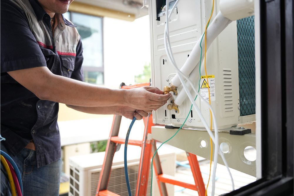 Man connects hoses to an air conditioning unit on a stand. Outdoor setting, focus on the unit. Man connects hoses to an air conditioning unit on a stand. Outdoor setting, focus on the unit.