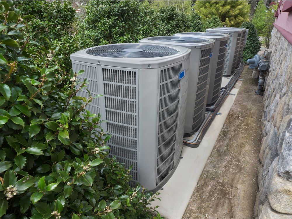 Four air conditioning units aligned, next to bushes, beside a stone wall. Four air conditioning units aligned, next to bushes, beside a stone wall.