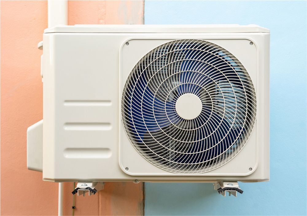 Exterior air conditioning unit mounted on a wall; white with a fan and colored wall background.