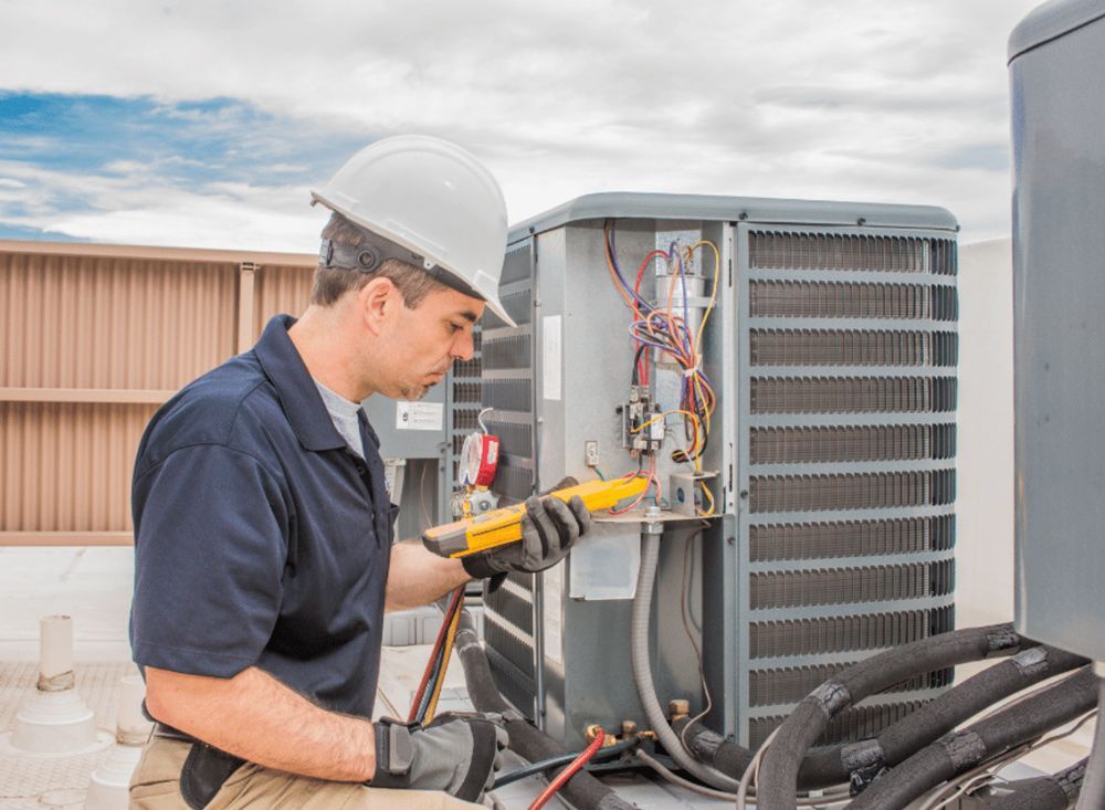 HVAC technician in a hard hat inspects air conditioning unit with a multimeter on a rooftop.