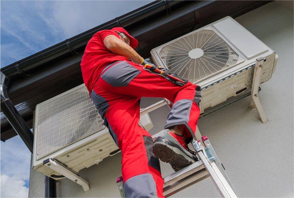 HVAC technician in red overalls on a ladder, working on an outdoor air conditioning unit mounted on a building. HVAC technician in red overalls on a ladder, working on an outdoor air conditioning unit mounted on a building.