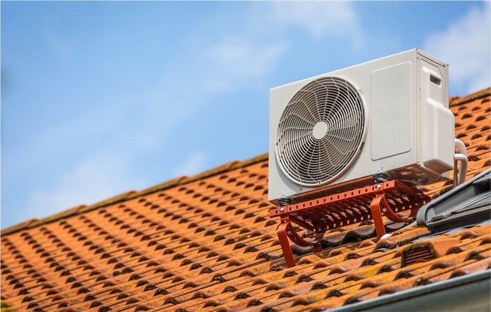 White air conditioning unit on a red tiled roof, blue sky background. White air conditioning unit on a red tiled roof, blue sky background.