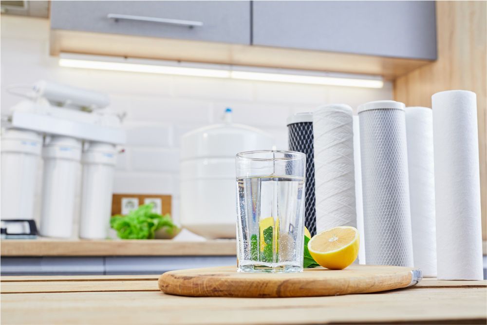 Glass of water with lemon on wood board, water filters in kitchen setting. Glass of water with lemon on wood board, water filters in kitchen setting.