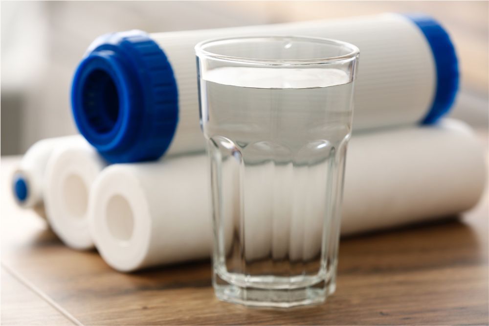 Glass of clear water beside three white and blue water filters.