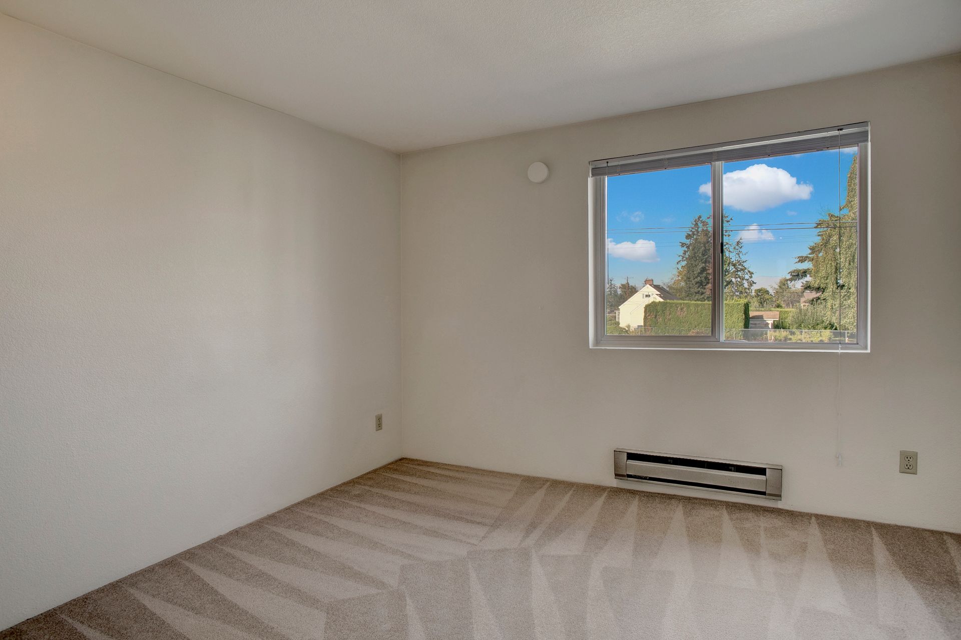 An empty bedroom with a large window and a carpeted floor.