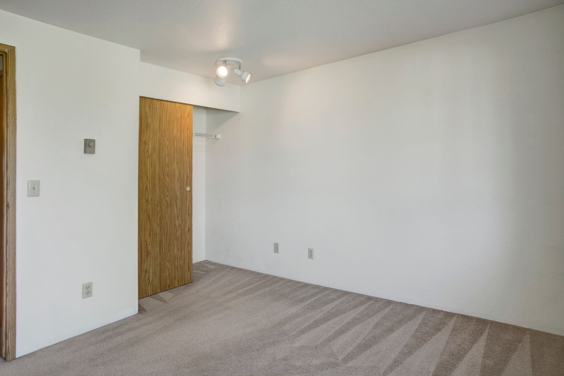 An empty room with a carpeted floor , white walls and a wooden door.