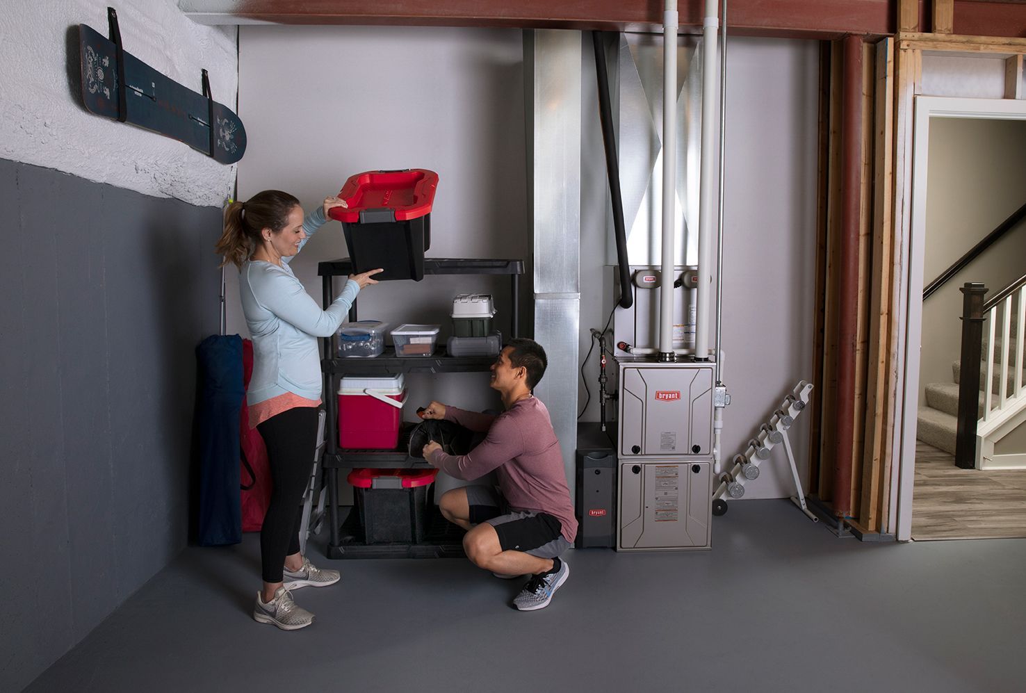 Couple organizing storage shelves in a basement with gray painted walls.