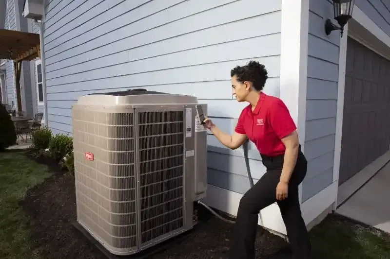 An HVAC repair woman in a red polo helping a home owners' unit. 