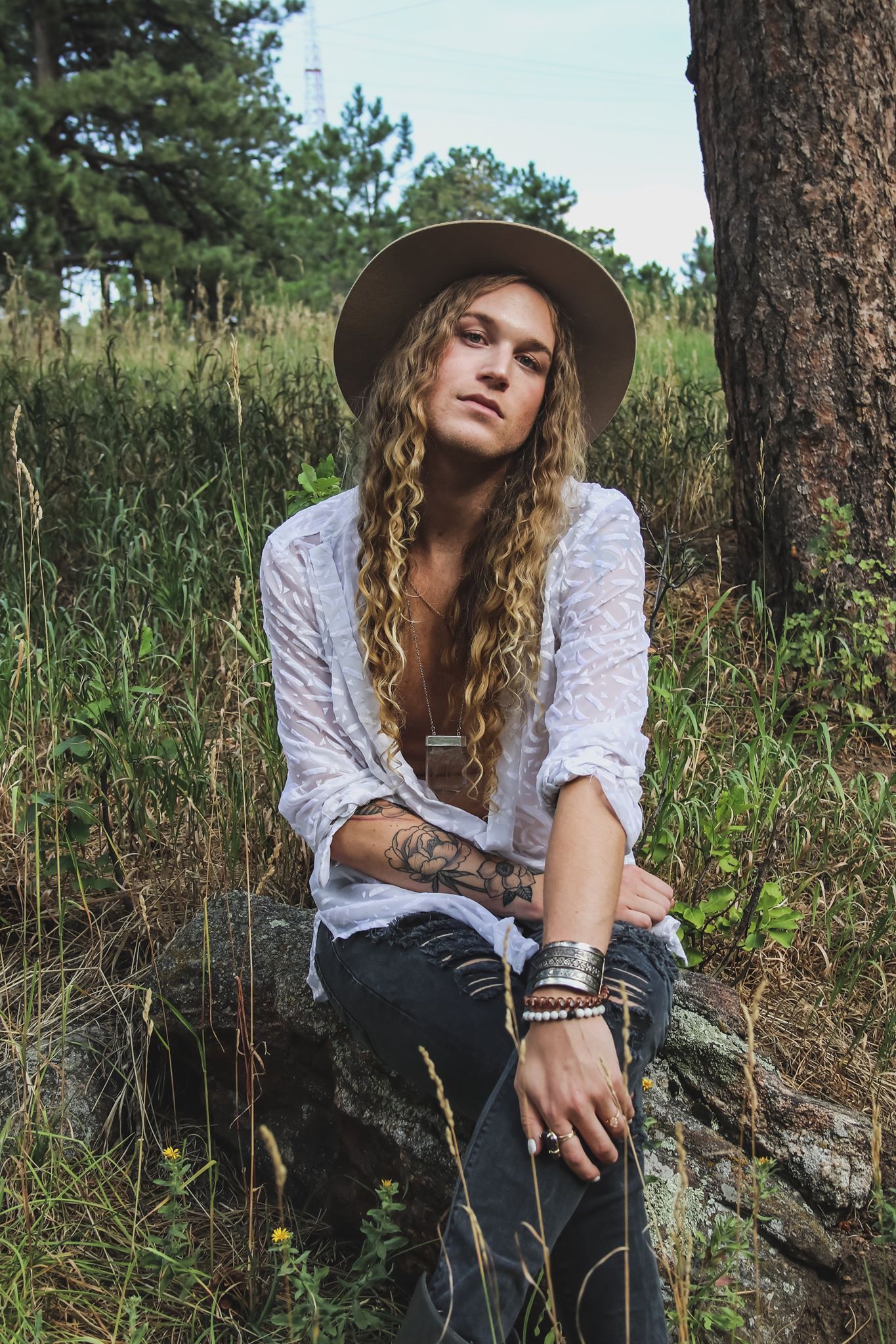 Scotty in a hat is sitting on a rock in the grass for a fashion photo shoot.