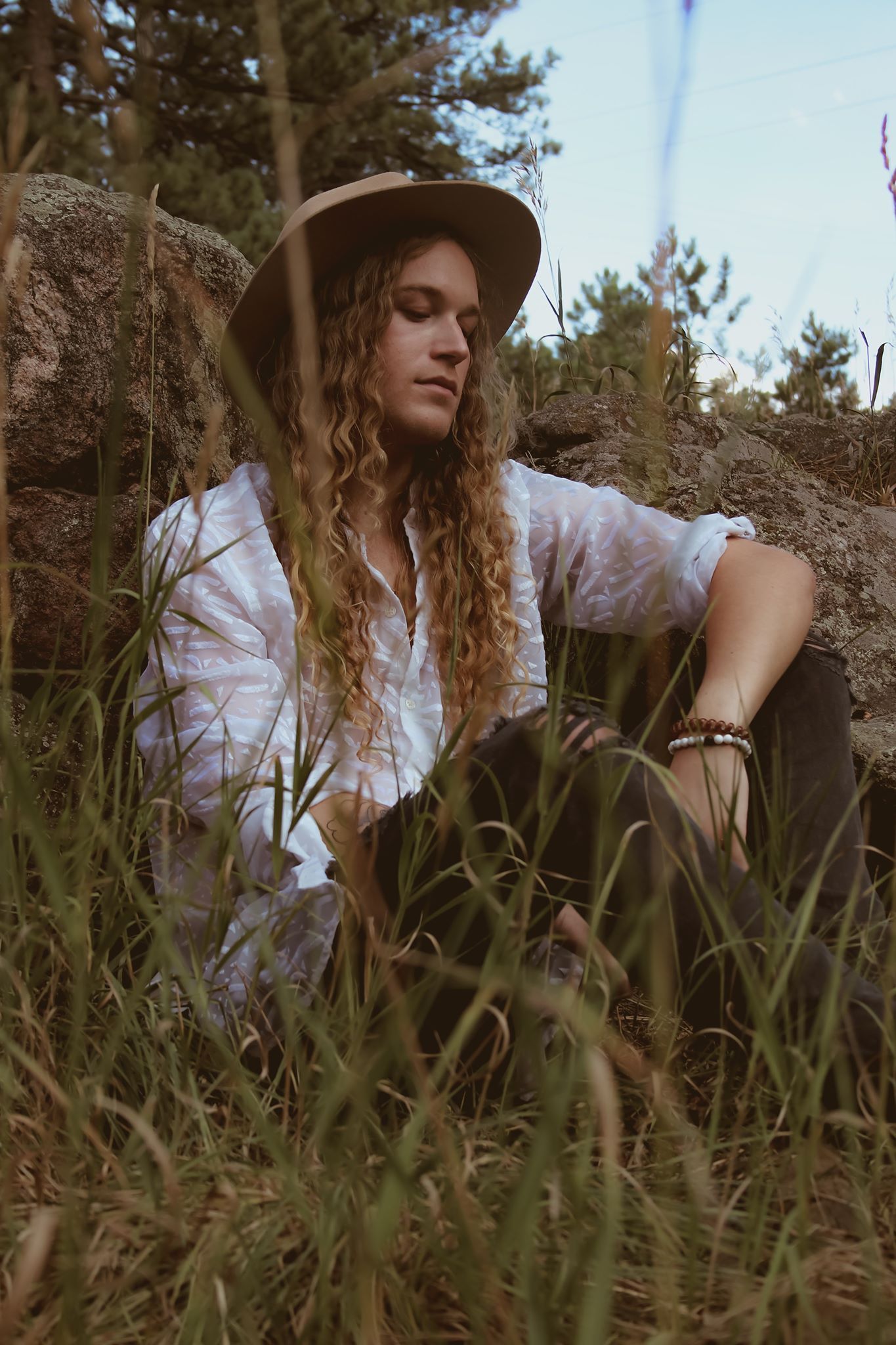 Scotty with long hair is sitting in the grass wearing a hat for a fashion photo shoot.