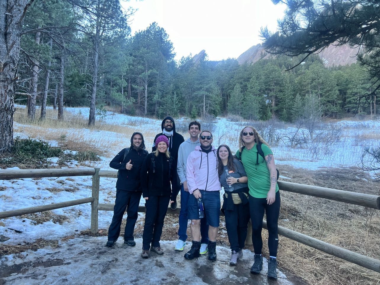 A group of people are standing next to a wooden fence in the snow.
