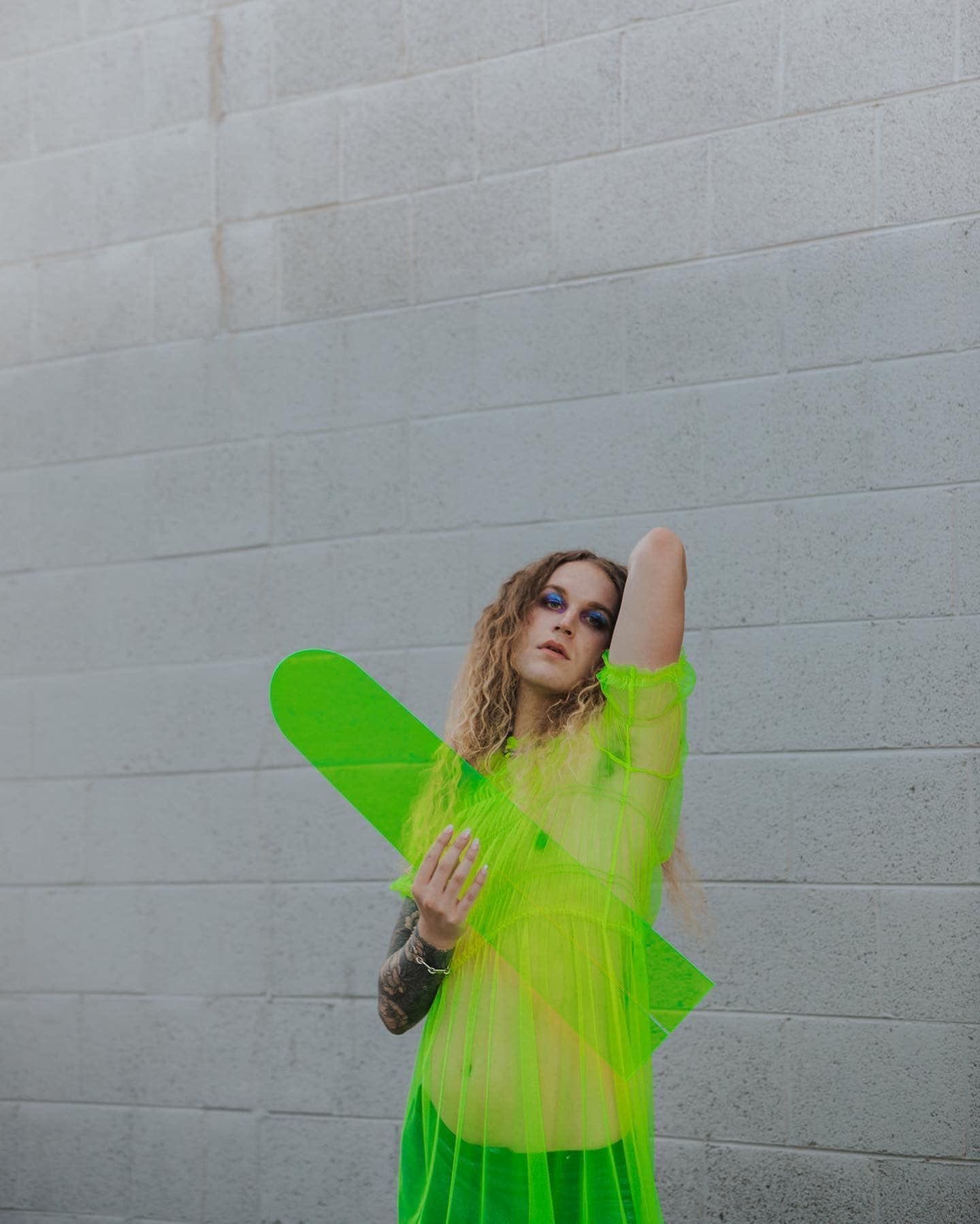 A woman in a neon green dress is standing in front of a brick wall for a fashion photo shoot.