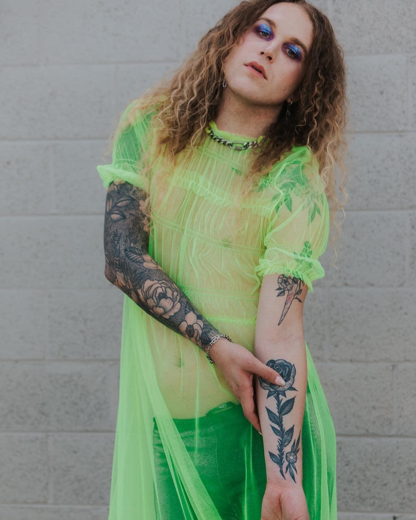 A woman with tattoos on her arms is wearing a neon green dress for a fashion photo shoot.