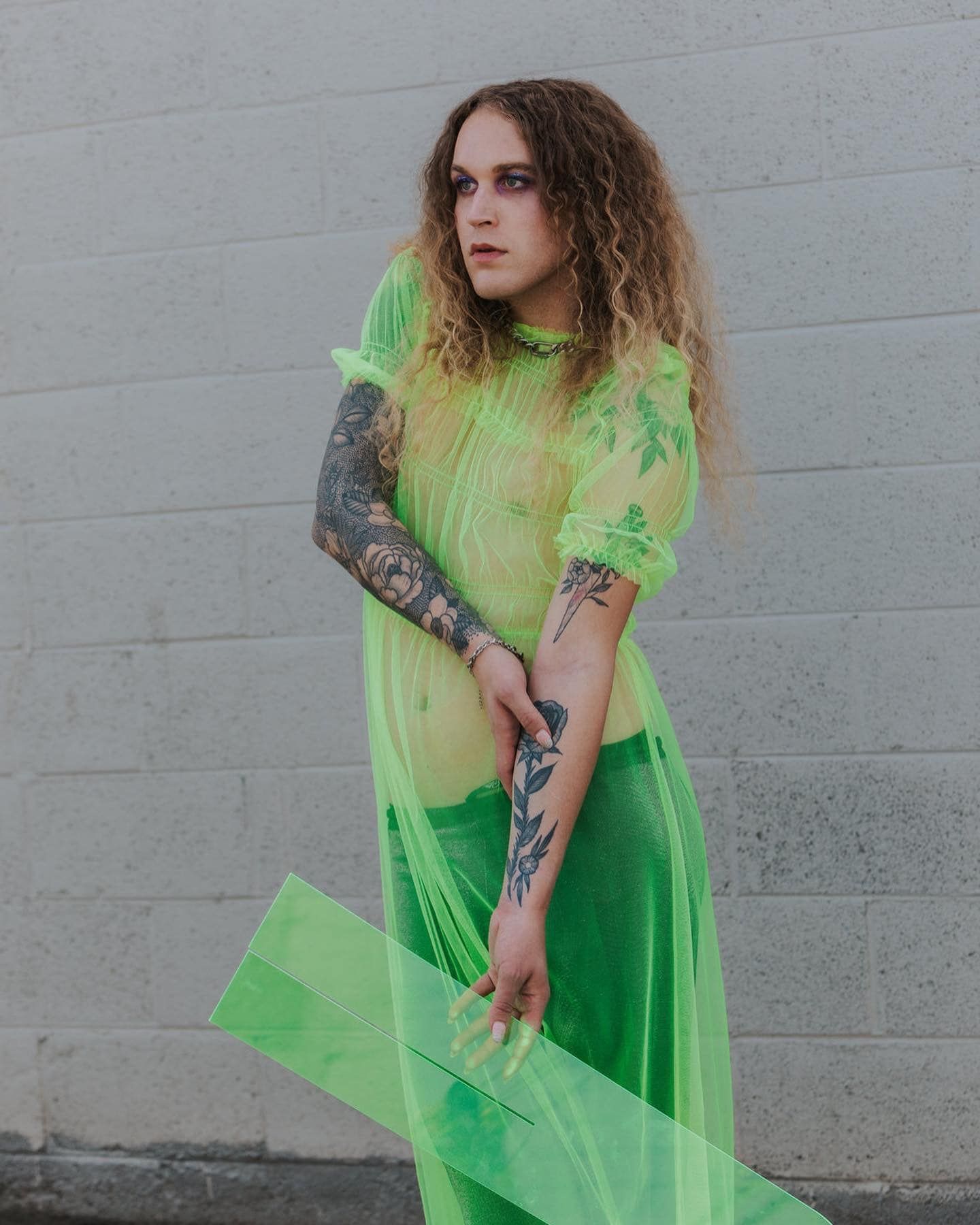 A woman in a neon green dress is standing in front of a brick wall for a fashion photo shoot.