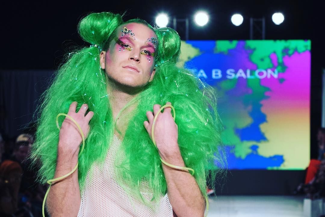 A woman with green hair is walking down a runway at a fashion show.