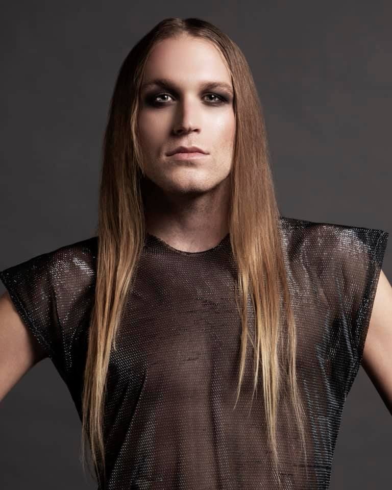 A man with long hair is wearing a black shirt for a photoshoot.