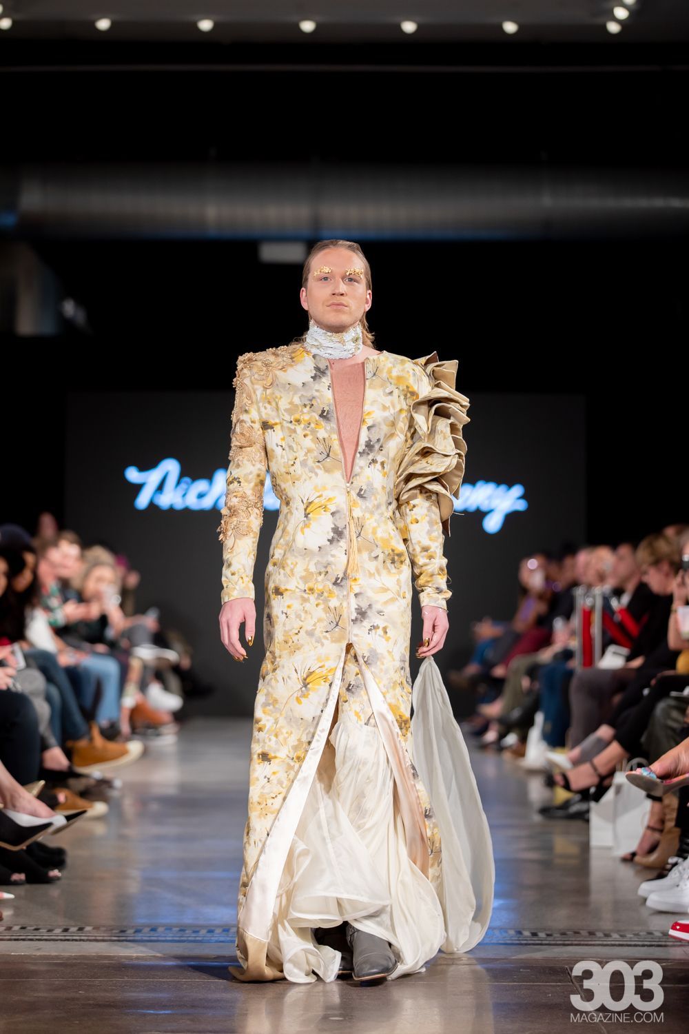A model is walking down the runway at a fashion show wearing a long dress.