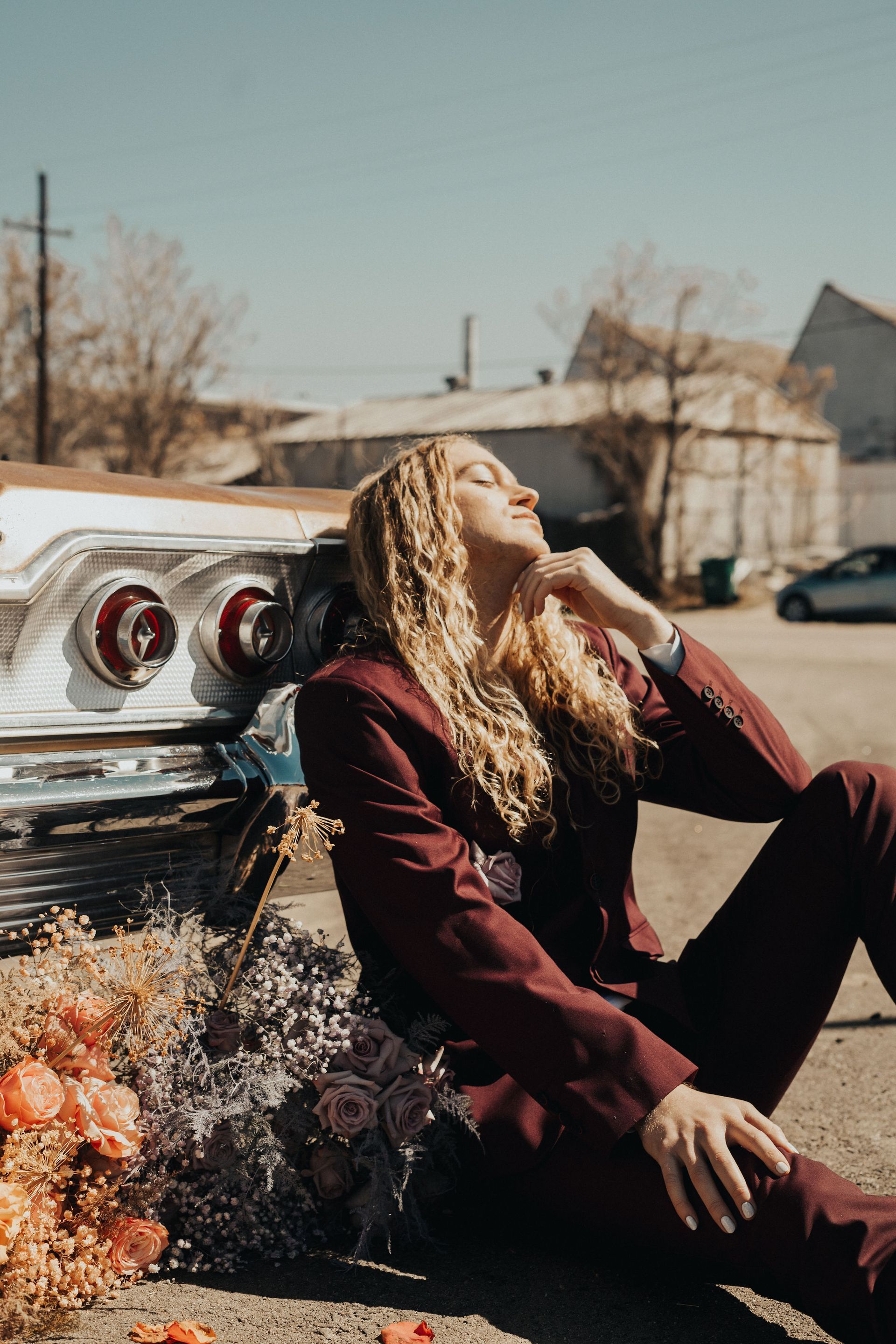 Scotty wearing a maroon suit posing in a car with flowers, modeling for a photoshoot