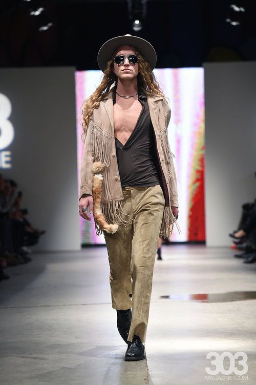 A man is walking down a runway wearing a hat and sunglasses.